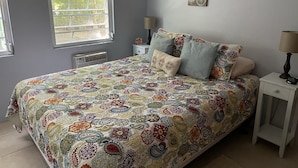 A bedroom with a large bed, two bedside tables, a window with blinds, and decorative wall art.