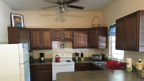 A kitchen with wooden cabinets, a white stove, a red kettle, a toaster, and a sink.