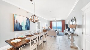 A spacious dining area with a wooden table and white chairs, a chandelier, and a large abstract painting on the wall. - Waterscape A603 ~ Top 10 View in Resort! 2 King Master Suites! (Fort Walton Beach)