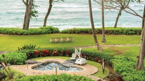 Un jardín ajardinado con un jacuzzi, sillas y vistas al océano.