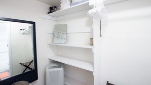Un bagno in bianco con uno specchio grande, un portascopini e uno scaffale con articoli da toilette.