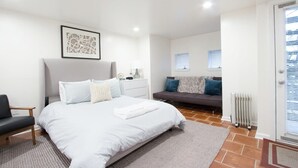Una camera da letto con un letto grande, un comodino, una sedia, un divano, un termosifone e una porta con finestra.