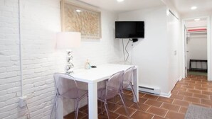 Un muro di mattoni bianchi, un tavolo bianco con sedie trasparenti, una TV a schermo piatto e un appendiabiti.