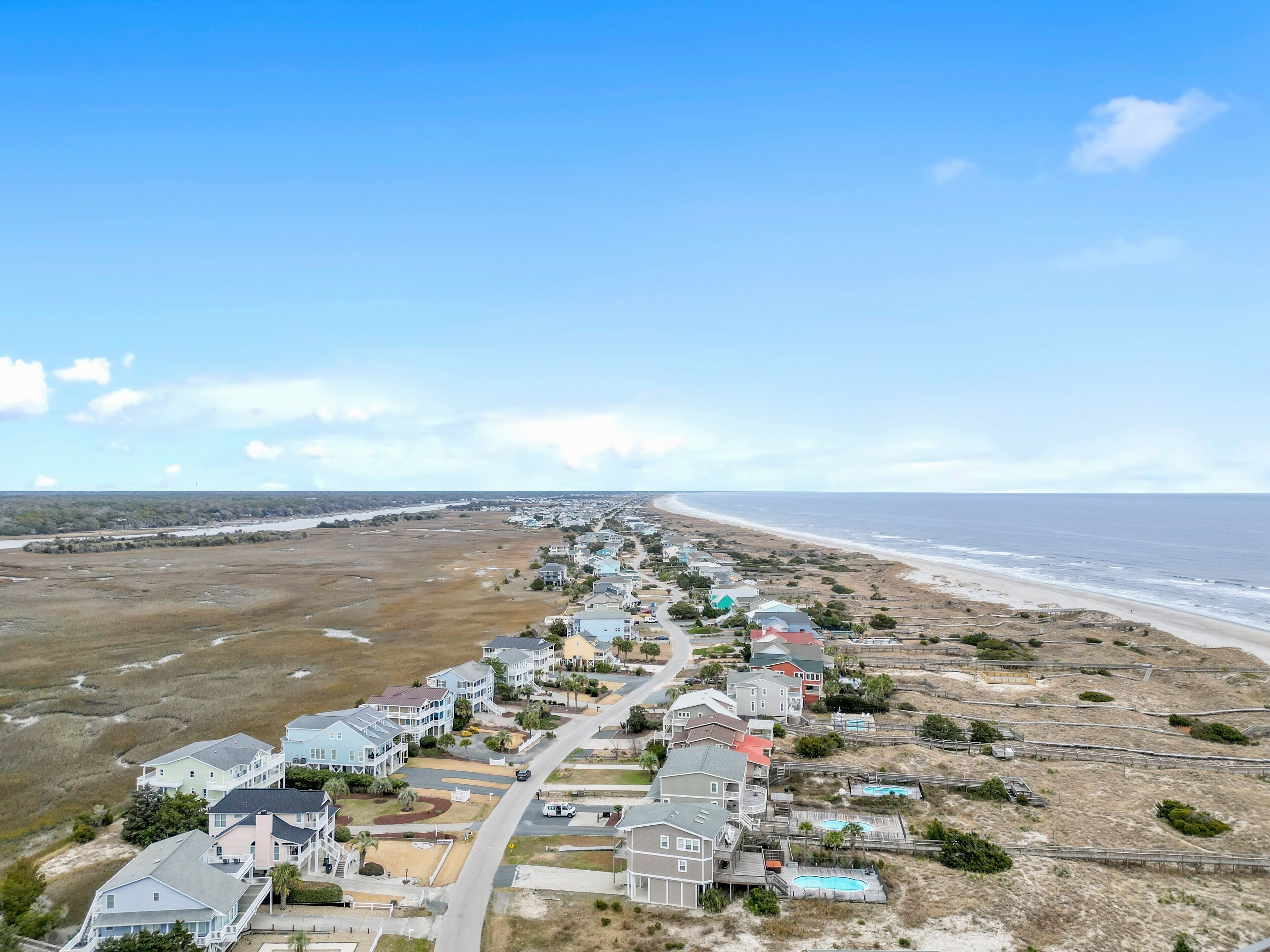 A coastal residential area with houses along the beach, a clear sky, and a view of the ocean.