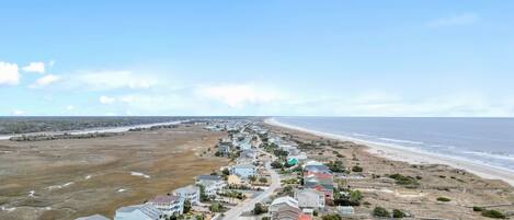 A coastal residential area with houses along the beach, a clear sky, and a view of the ocean.