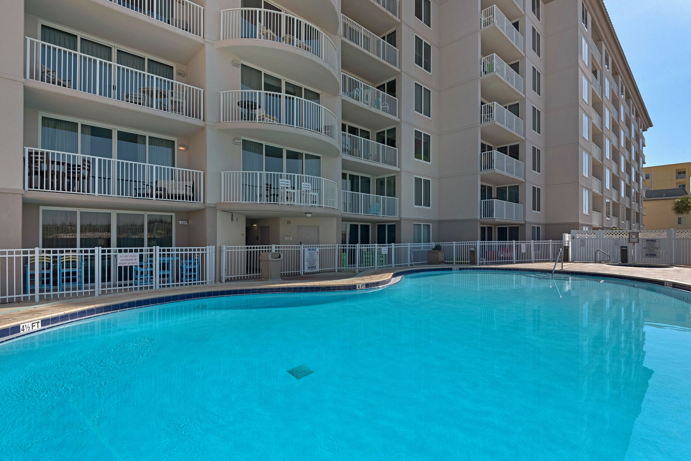 A swimming pool adjacent to a multi-story building with balconies.