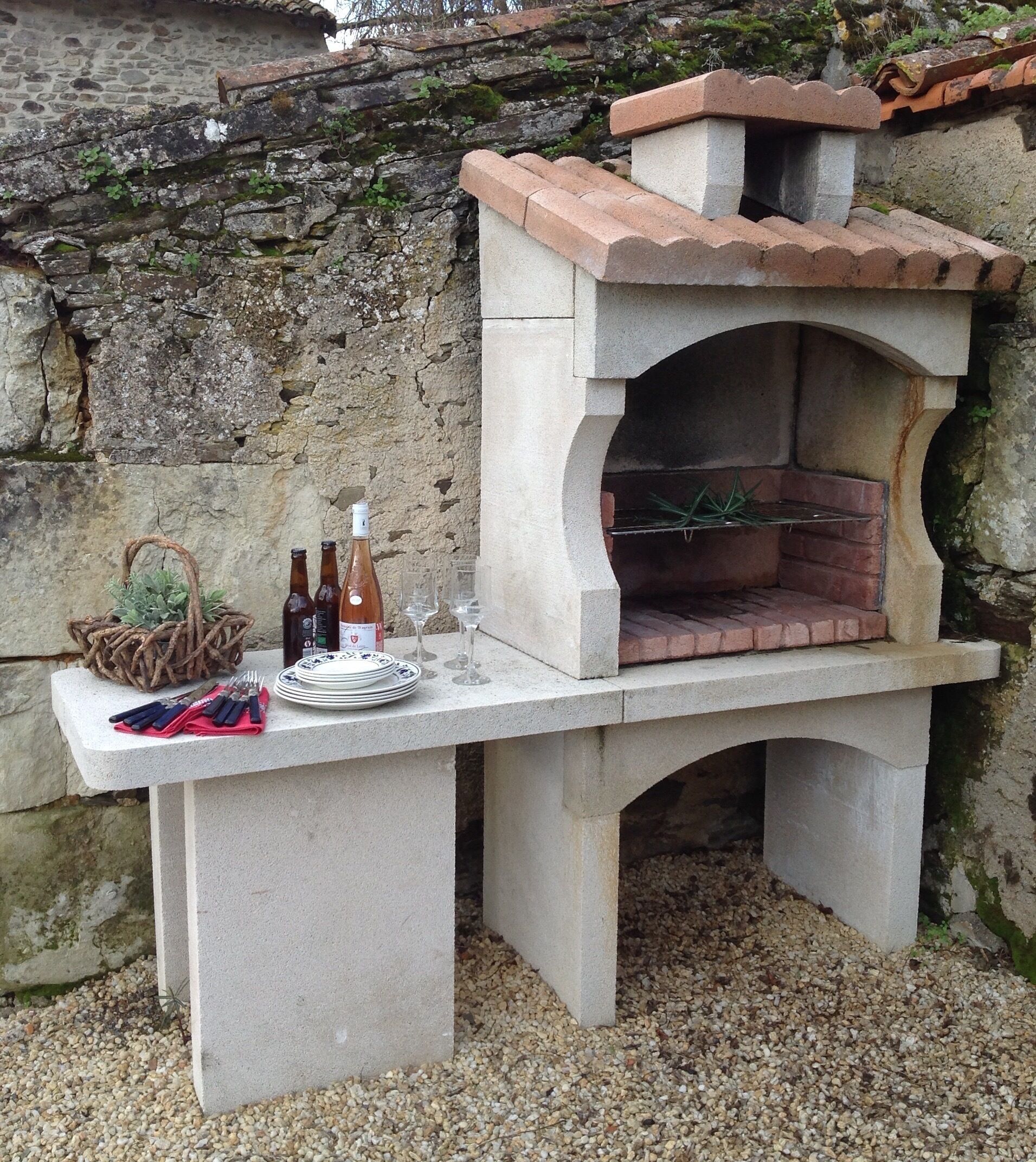 Un four à pizza extérieur en pierre, avec un toit en briques, une table avec des assiettes, des couverts et des bouteilles de vin.