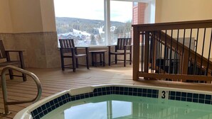 Zona de piscina con vistas a un paisaje nevado, una terraza de madera y una escalera.