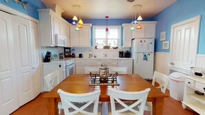 A kitchen with white cabinets, a wooden dining table, and colorful pendant lights. - Golf Cart Included, Shared Pool, Pet Friendly, Boardwalk to Beach (Port Aransas)
