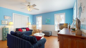 A living room with a blue wall, a ceiling fan, a sofa, a coffee table, and a wooden cabinet. - Golf Cart Included, Shared Pool, Pet Friendly, Boardwalk to Beach (Port Aransas)