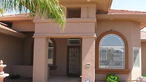 A two-story house with a beige facade, a large arched window, and a door with a decorative metal gate. - Spacious 4BR Coyote Ranch Retreat with Private Pool & RV Parking in Casa Grande (Casa Grande)