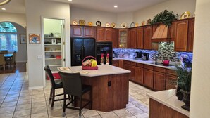 A kitchen with wooden cabinets, a central island, and a dining area with chairs. - Spacious 4BR Coyote Ranch Retreat with Private Pool & RV Parking in Casa Grande (Casa Grande)