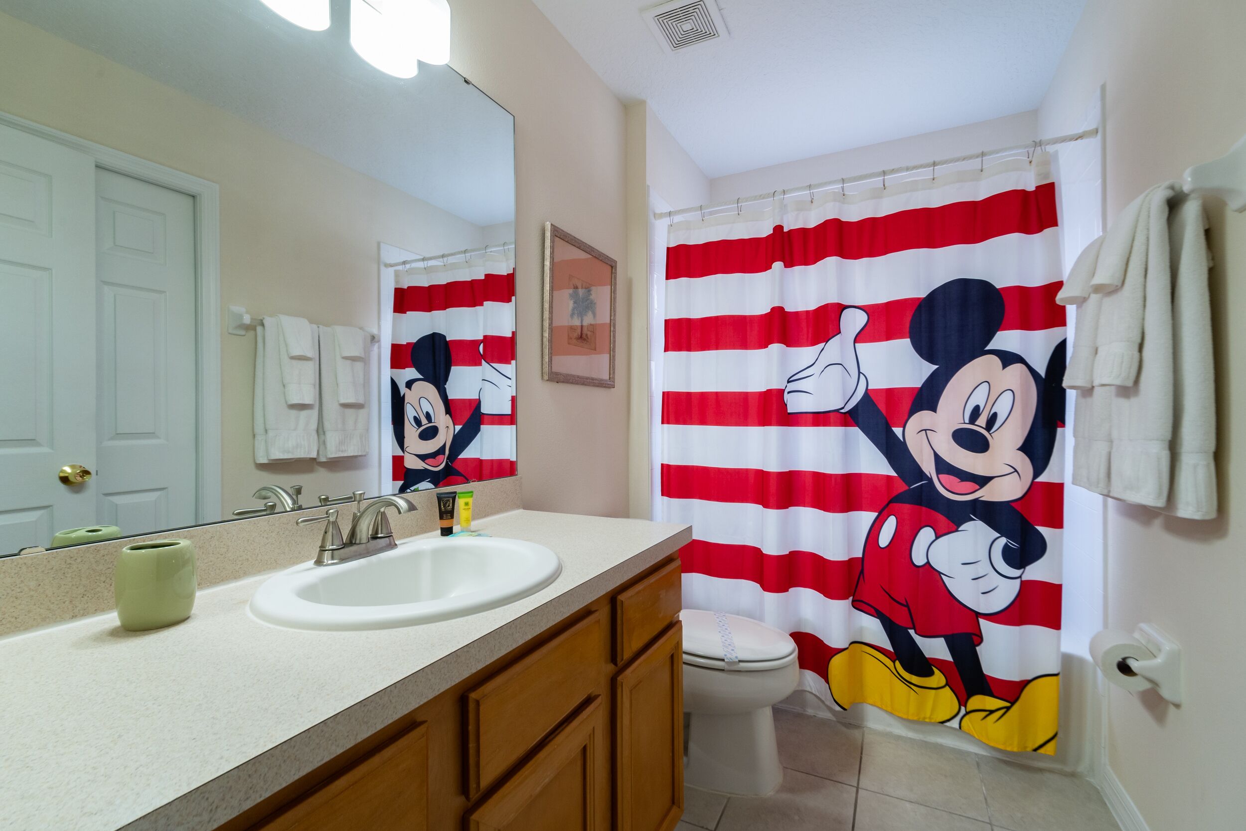 A bathroom with a Mickey Mouse shower curtain, a white sink, and wooden cabinets.