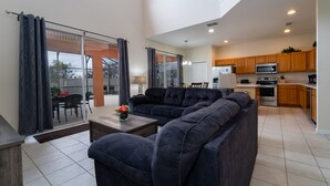 A modern living room with a sectional sofa, a dining table, and a kitchen area with wooden cabinets and appliances.
