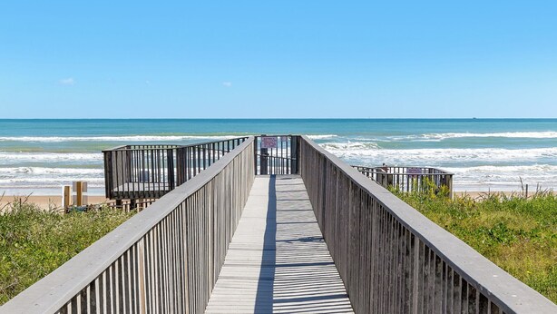 Un muelle de madera que conduce a la playa, con vista despejada al océano.
