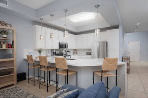 A modern kitchen with white cabinets, a central island with bar stools, stainless steel appliances, and pendant lighting.