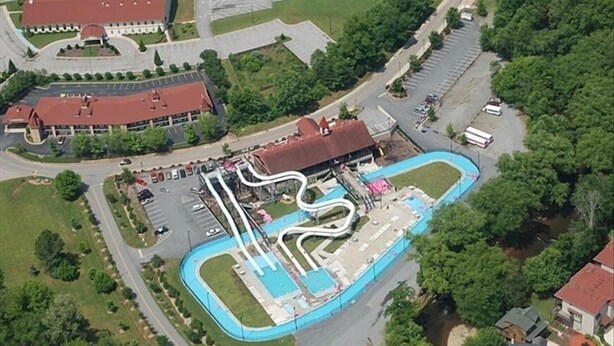 Una vista aerea di un parco con uno scivolo acquatico tortuoso, un parcheggio e un edificio con tetto rosso.