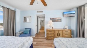 A hotel room with two beds, a desk, a TV, and a view of the beach.