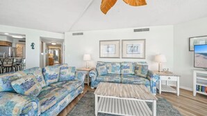 A living room with a sofa set, a coffee table, two lamps, and framed pictures on the wall. - Welcome to Turtle Tracks on beautiful Panama City Beach.  Book Today! (Panama City Beach)