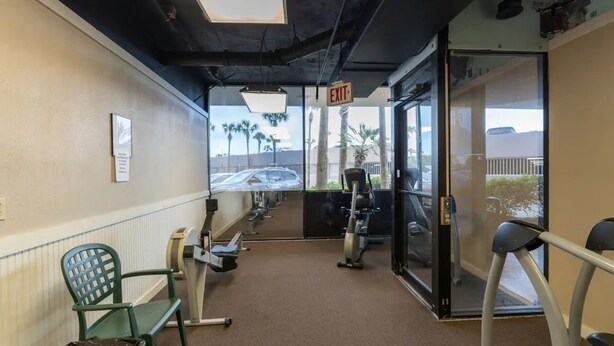 A gym with exercise equipment, an exit sign, and a view of palm trees and a car through the glass door. - Welcome to Turtle Tracks on beautiful Panama City Beach.  Book Today! (Panama City Beach)