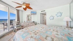 A hotel room with a large bed, a ceiling fan, a TV, a balcony with a view of the ocean, and a dresser with a mirror. - Welcome to Turtle Tracks on beautiful Panama City Beach.  Book Today! (Panama City Beach)