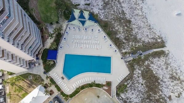 An aerial view of a resort with a swimming pool, sun loungers, and a beach area.