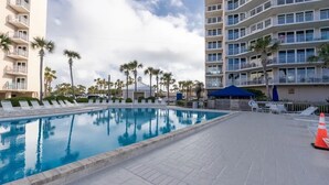 A swimming pool area with lounge chairs, palm trees, and a multi-story building with balconies. - Welcome to Turtle Tracks on beautiful Panama City Beach.  Book Today! (Panama City Beach)
