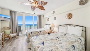 A hotel room with two beds, a ceiling fan, a television, a chair, and a balcony with a view of the sea. - Welcome to Turtle Tracks on beautiful Panama City Beach.  Book Today! (Panama City Beach)