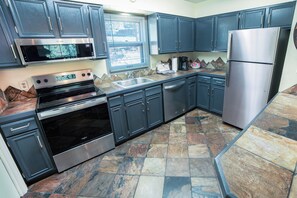A modern kitchen with stainless steel appliances, dark cabinetry, and a stone tile backsplash.