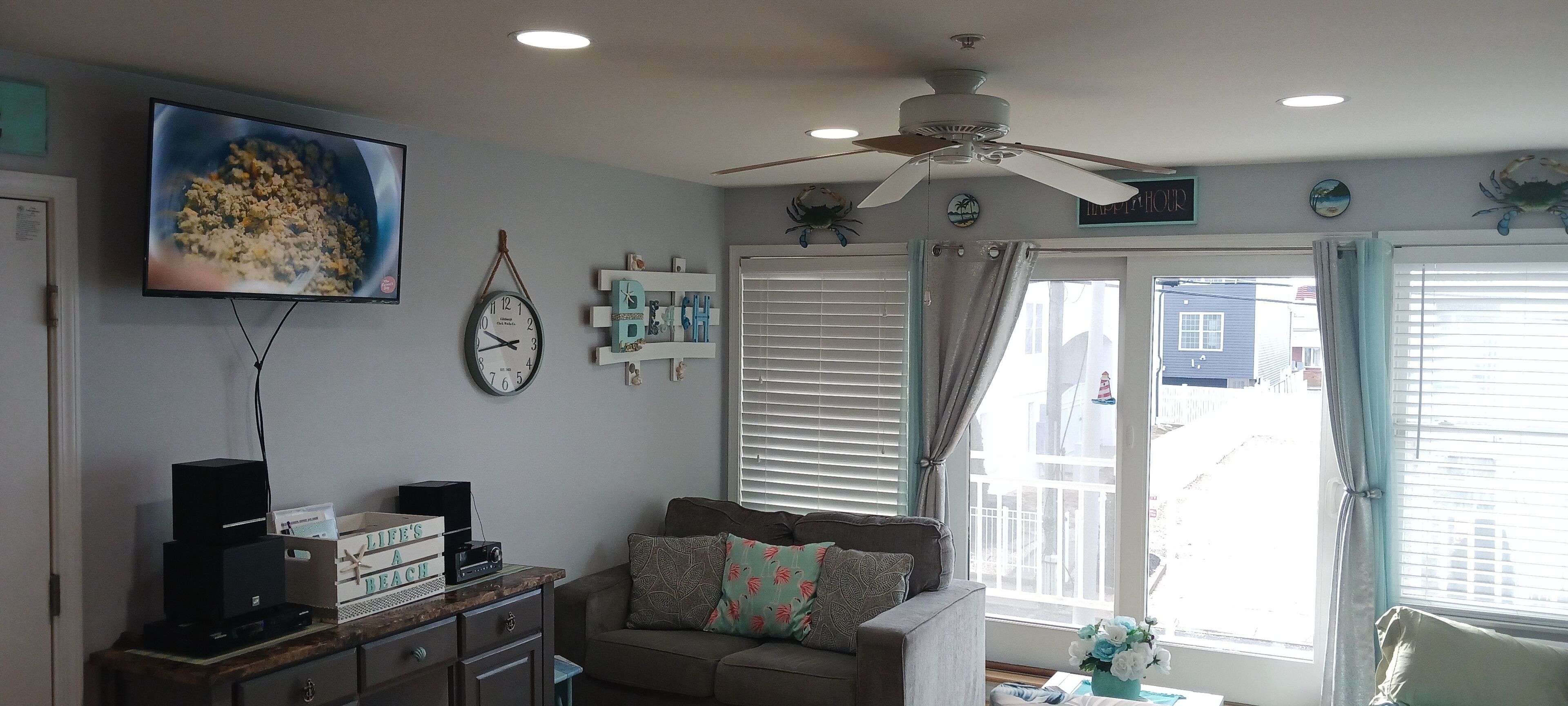 A living room with a television, clock, ceiling fan, and a window with curtains.