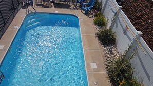 Una piscina rectangular con agua azul cristalina, rodeada por un suelo de hormigón y una pared blanca con un letrero que dice 'No Diving'.