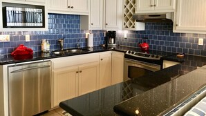 A modern kitchen with white cabinets, a black countertop, stainless steel appliances, and blue backsplash tiles.