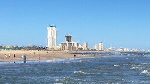 A beach with a city skyline in the background, including tall buildings and a clear sky.