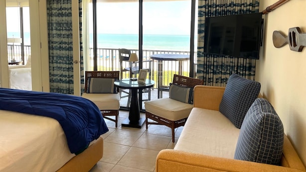 A hotel room with a balcony, a bed, a sofa, a table, and a TV.
