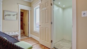 Ein Zimmer mit einem Bett, einer gepolsterten grünen Bank, einem gerahmten Kunstwerk, einer zur Toilette führenden Tür und einem gefliesten Boden.