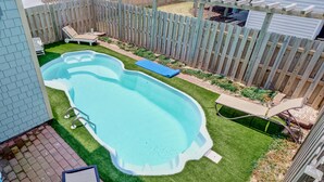 Un patio trasero con piscina, terraza de madera y zona amurallada.