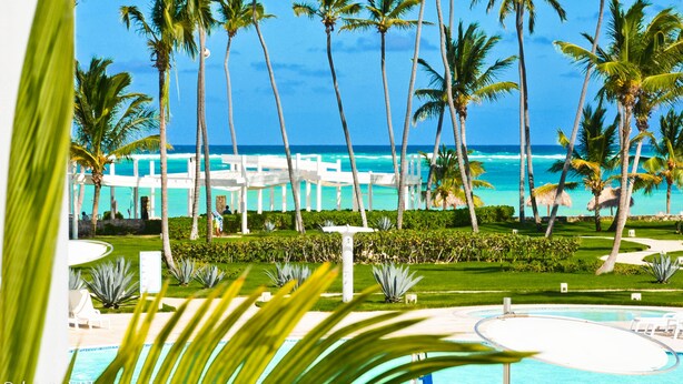 A resort with a pool, palm trees, and a view of the ocean. - Playa Turquesa Luxury Beach Front Condo with Ocean View and Much More (Bávaro)