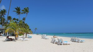 A beach with white lounge chairs and palm trees. - Playa Turquesa Luxury Beach Front Condo with Ocean View and Much More (Bávaro)