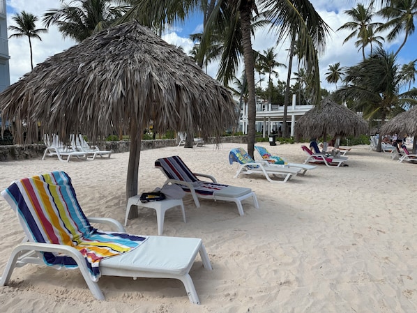 A beach with white lounge chairs, some with colorful towels, and thatched umbrellas.
