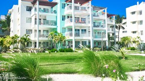 A multi-story hotel with balconies, a well-maintained lawn, and palm trees. - Playa Turquesa Luxury Beach Front Condo with Ocean View and Much More (Bávaro)