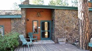 Una cabaña de madera con fachada de piedra, dos puertas y una terraza con sillas.