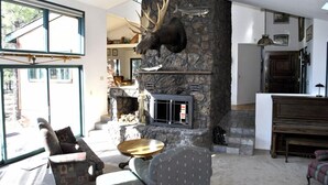 Una sala de estar con chimenea de piedra, cabeza de alce montada y un piano.