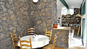 Un comedor con pared de piedra, sillas de madera, una mesa redonda y una estantería llena de libros.