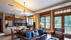A spacious living room with a leather sofa, a dining area with a wooden table, and large windows offering a view of the outdoors.
