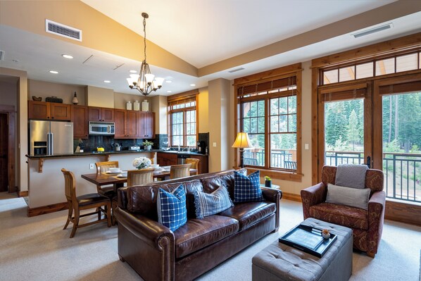 Un salón espacioso con un sofá de cuero, un comedor con mesa de madera, y ventanas amplias que ofrecen vistas al exterior.
