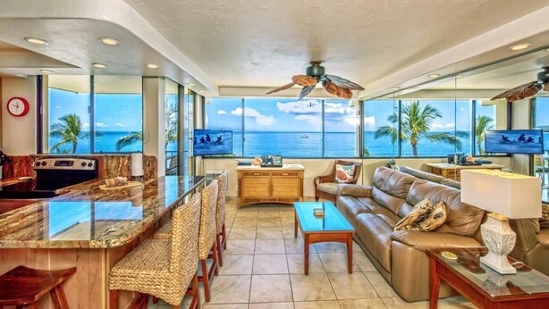 A spacious living area with a large window overlooking the ocean, a kitchen with a modern stove, and a comfortable seating area with a sofa and chairs.