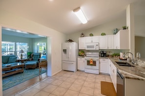 A modern kitchen with white cabinets, a refrigerator, microwave, oven, and a sink. There is a dining area with a table and chairs.