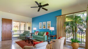 A spacious living room with a blue accent wall, a ceiling fan, and a large window with curtains. - Kapalua Bay Villa 14B1 | Coastal Vibes & Ocean Views (Lahaina)