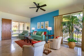 Uma sala de estar espaçosa com uma parede azul decorativa, um ventilador de teto e uma janela grande com cortinas.