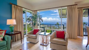A spacious room with two armchairs, a small table, and a view of the ocean through large windows. - Kapalua Bay Villa 14B1 | Coastal Vibes & Ocean Views (Lahaina)